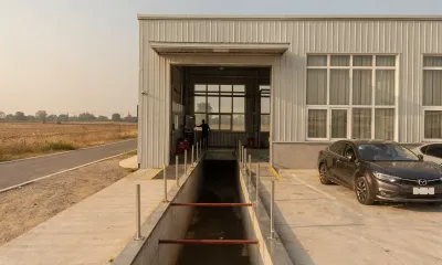 Nave de una estación de inspección junto a una carretera comarcal, con el campo al fondo y dos turismos aparcados