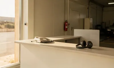 Mostrador de recepción con el teléfono fijo y unos auriculares apoyados, con luz de mañana entrando por la cristalera
