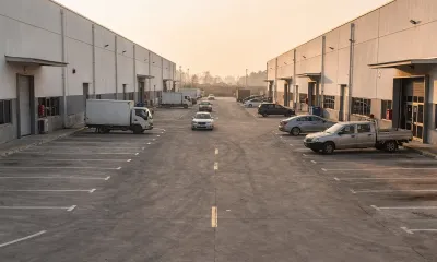 Avenida de un polígono industrial vista desde el aparcamiento de una estación, con otras naves al fondo